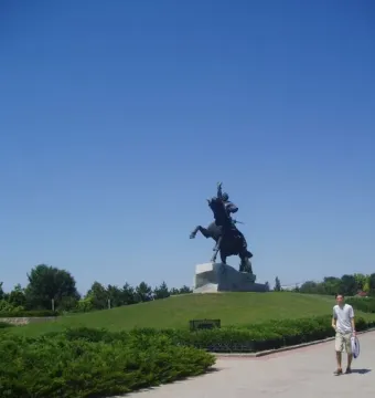 Suvorov Monument, a dark equestrian statue on a light stone pedestal above a grassy mound with a person walking nearby.
