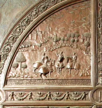 Close-up of a bronze gate relief showing horsemen in a historical landscape with Latin inscription and decorative scrollwork.