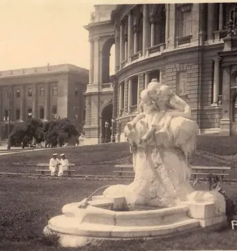 Children and Frog fountain sculpture in a public square with classical buildings in the background.