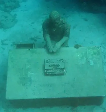 The Lost Correspondent underwater sculpture at Molinere Underwater Sculpture Park, showing a seated figure at a desk with a typewriter on the seabed.
