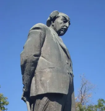 Monument to Avetik Isahakyan showing a dark statue of a man in a suit holding a cane against a blue sky.