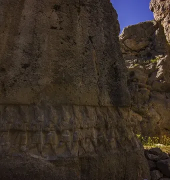 Yazılıkaya rock reliefs carved along a large stone wall in a narrow passage with sky visible above.