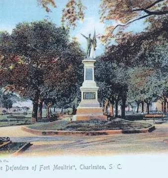 The Defenders of Fort Moultrie monument in a tree-filled park, with a tiered stone base and a figure holding a flag on top.