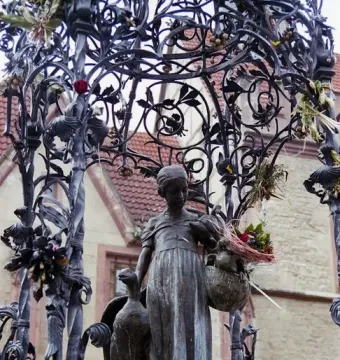 Gänseliesel Fountain bronze statue of a girl holding a goose and a basket of flowers beneath an ornate canopy.