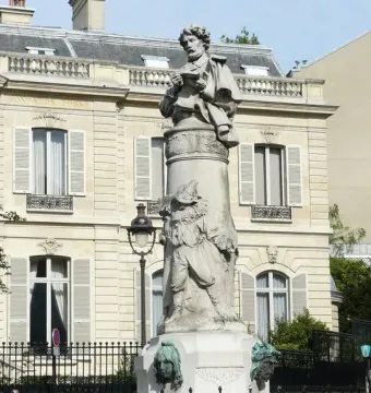 Gavarni Fountain with a stone column topped by a figure holding a book, with relief sculpture and sculpted heads at the base.