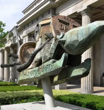 Humpty-Dumpty Machine bronze sculpture with green patina and machine-like components in front of a classical building