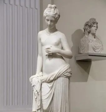 Pandora marble statue of a standing woman holding a small object, with drapery around her lower body.