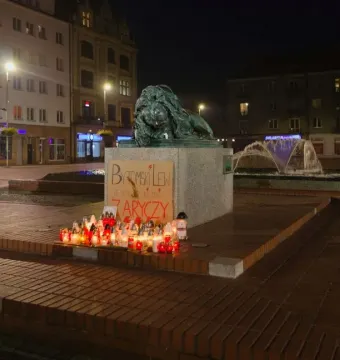 Sleeping Lion sculpture on a pedestal with candles and a sign arranged below it at night.