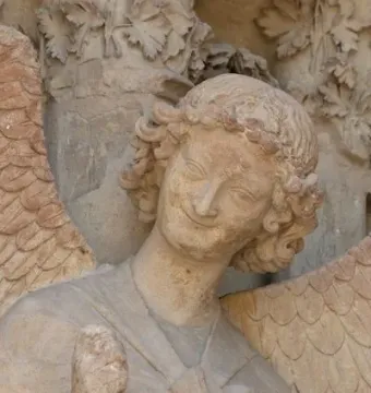 Smiling Angel sculpture with curly hair, a gentle smile, and raised arm on Reims Cathedral