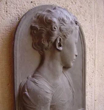 Bust of a child in gray stone relief, shown in profile with curly hair and draped clothing.