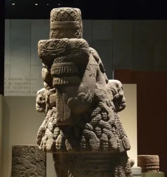 Left-side view of the Coatlicue stone sculpture, showing its carved skulls, necklace, and textured skirt-like body.