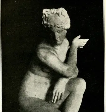 Crouching Venus statue in a crouching pose on a carved pedestal.
