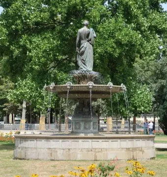 Diana Fountain seen from behind beside a stone basin and circular pool, surrounded by trees and greenery.