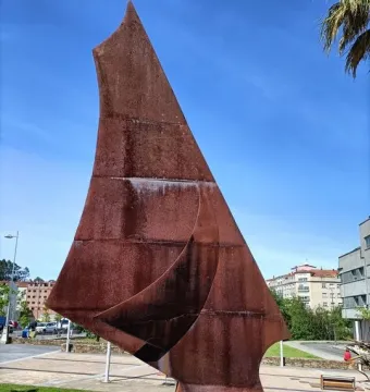 Dorna, a large abstract reddish-brown metal sculpture in an outdoor plaza with landscaping and city buildings behind it.