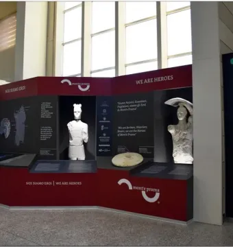 Two Giants of Mont\'e Prama statues displayed in a red and black exhibition stand.