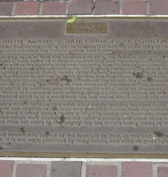 A metal plaque with engraved text rests in a red-brick paved surface.