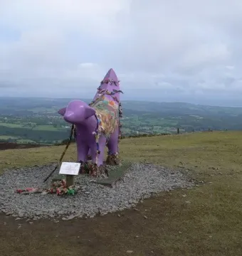 Superlambanana sculpture covered in colorful ribbons and fabric on a grassy hill