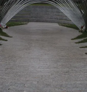 Infinite Wave memorial with arched metal bars forming a tunnel-like walkway beside a curved stone wall.