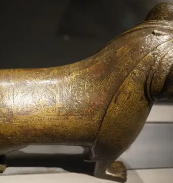 The Lion of Monzon sculpture shown from a three-quarters angle, with engraved decorative patterns across its body.