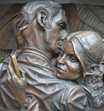 The Meeting Place bronze sculpture showing a man kissing a woman’s forehead in a close embrace.