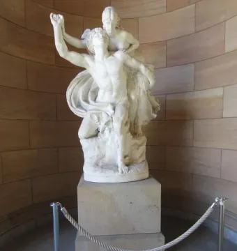 Mercury and Psyche white stone sculpture on a pedestal beside a curved tan stone wall.