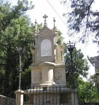Stone monument from the Monumental Rosary of Montserrat with a central religious relief, a dove, and a cross above it, surrounded by a low fence.
