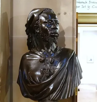 The Nubian Man, a dark metallic bust with detailed hair, facial hair, and draped garments on a pedestal.