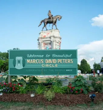 The Robert E. Lee Monument stands on a tall stone base covered in graffiti, with a green Marcus-David Peters Circle sign in the foreground.