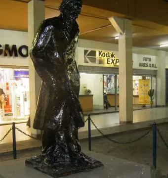 Monument to César Vallejo on a low concrete base at night, with lit storefronts behind it.