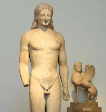 Kouros marble statue of a nude male figure with long hair, missing the right forearm, with a winged sphinx sculpture behind it.