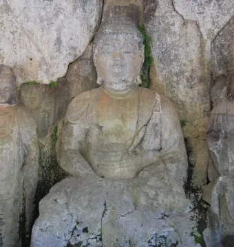 Three weathered stone Buddhas carved into a light grey cliff face at Usuki Stone Buddhas.