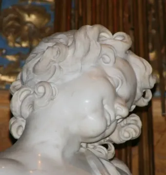 Close-up of the Ecstasy of Saint Teresa sculpture showing a white marble face with curled hair and a serene expression.