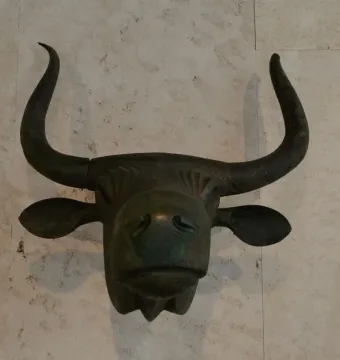 Toros de Costitx bronze bull head sculpture with curved horns and stylized features against a light wall.