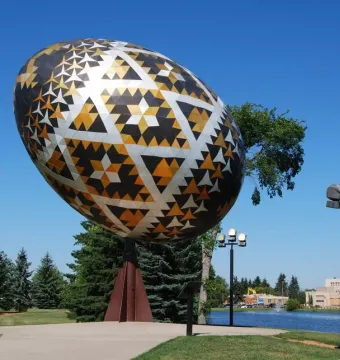 The Vegreville Pysanka egg sculpture with gold, black, and silver geometric patterns beside a pond and trees.