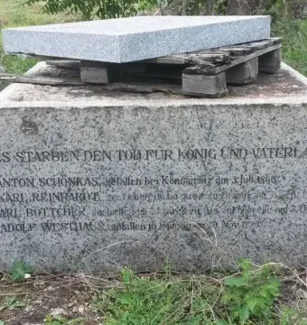Weathered stone base of the Dreyse Monument with German inscriptions, topped by a wooden pallet and granite slab.