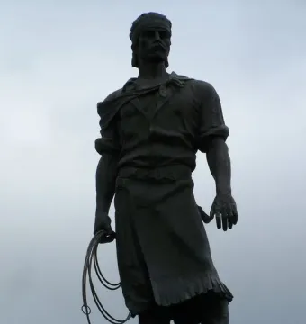Laçador statue of a man holding a coiled lasso against an overcast sky.