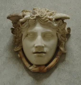 Medusa Rondanini marble head with curly hair and wing-like elements against a grey wall.