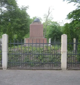Napoleonstein stone monument behind a dark metal fence in a leafy park.