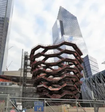 The Vessel rises among glass skyscrapers, with a chain-link fence and Gate 14 sign in the foreground.