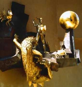 The Defender of Time sculpture with a golden figure, clock, rooster, and creature mounted on a wall.