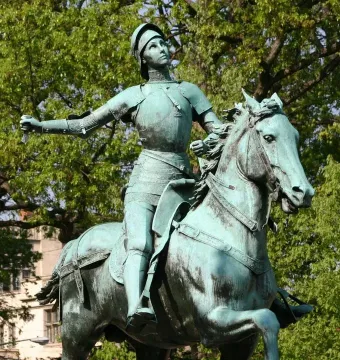 Joan of Arc equestrian statue in oxidized bronze, with an armored figure holding a sword hilt on a rearing horse.