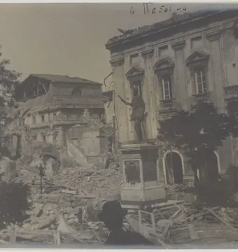 John of Austria statue on a tall pedestal amid rubble beside a damaged building