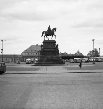 King Johann Memorial equestrian statue on a stone pedestal in a city square with buses and pedestrians nearby.