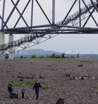Visitors climb the stairway of the Tetrahedron steel lattice structure, with children exploring the rocky base below.