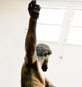 The Artemision Bronze seen from the side and back, with one arm raised and the other extended.