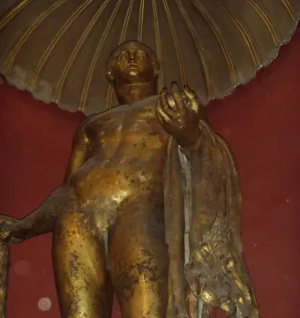 Weathered bronze statue of Hercules standing nude, holding a staff and apples with an animal skin draped over one arm.