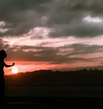 La Madre del emigrante silhouetted against a colorful sunset over the sea.