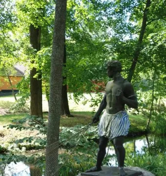 Morianbron sculpture standing on a boulder beside a stream with a rope and wooden walkway nearby
