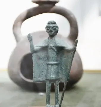 Nuragic bronze statuette of a tribal chief with a raised arm and staff, mounted on a wooden base.