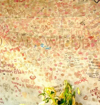 Oscar Wilde’s tomb covered with lipstick imprints, handwritten messages, and drawings, with flowers at the base.
